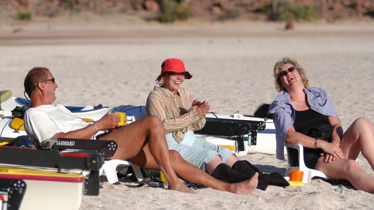 Travelers relaxing and laughing on a sandy beach in Loreto after a day of kayaking in Baja Mexico, enjoying the perfect mix of adventure and leisure on a Mexico kayak tour.
