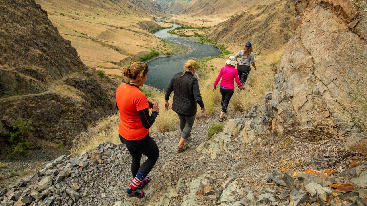 Group of hikers walking along a rocky trail above the Salmon River in Idaho, combining outdoor wellness travel with the excitement of rafting adventures.