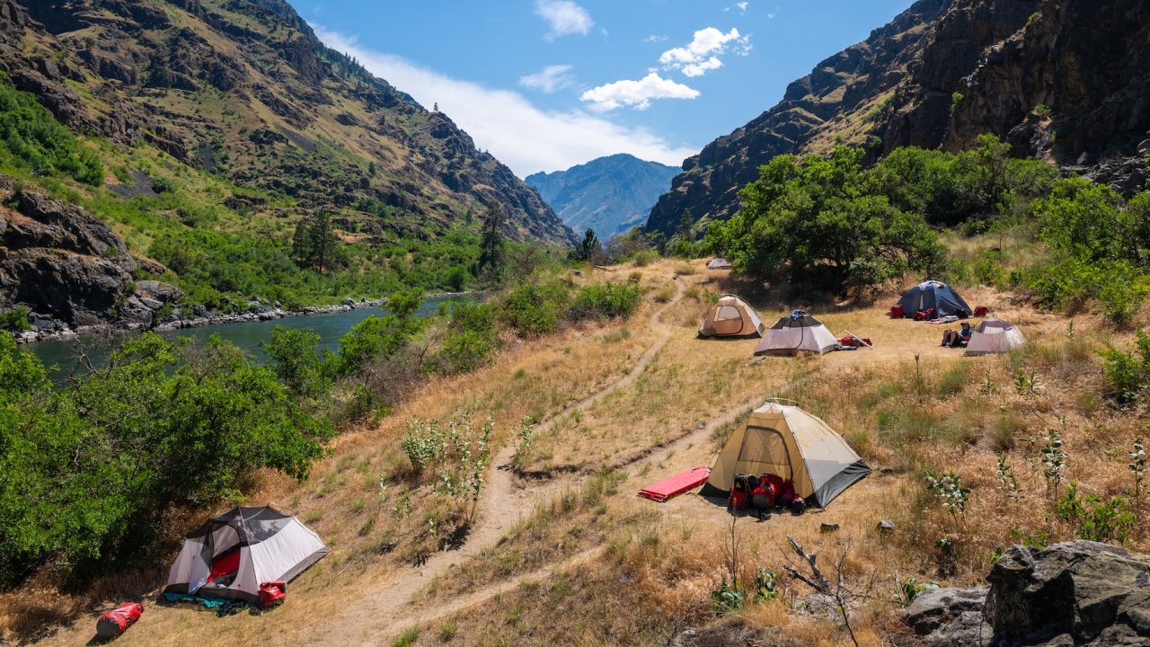 Riverside campsite with tents set up along the Salmon River in Idaho, offering a rejuvenating wellness retreat paired with whitewater rafting adventures.