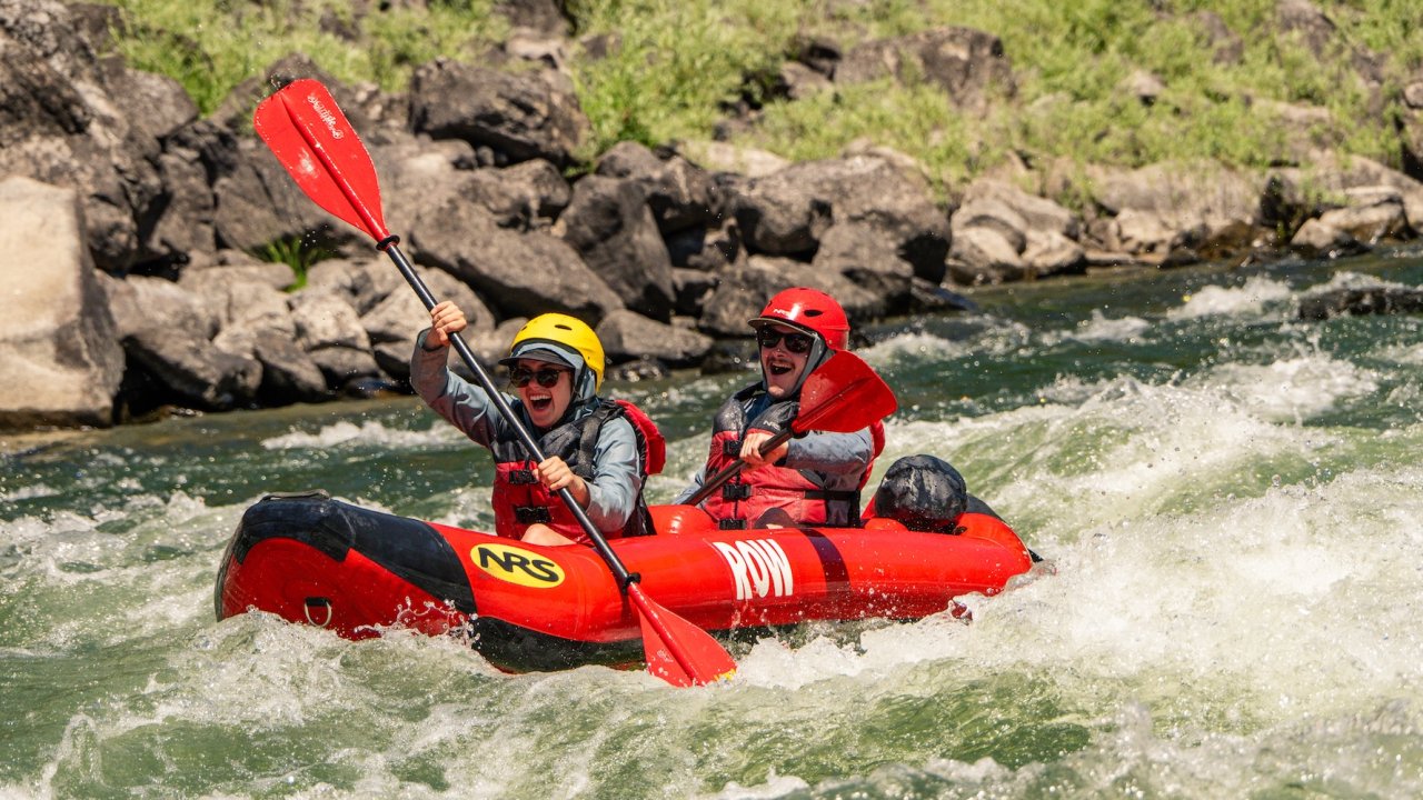 Two paddlers smiling while navigating splashy rapids in an inflatable raft.
