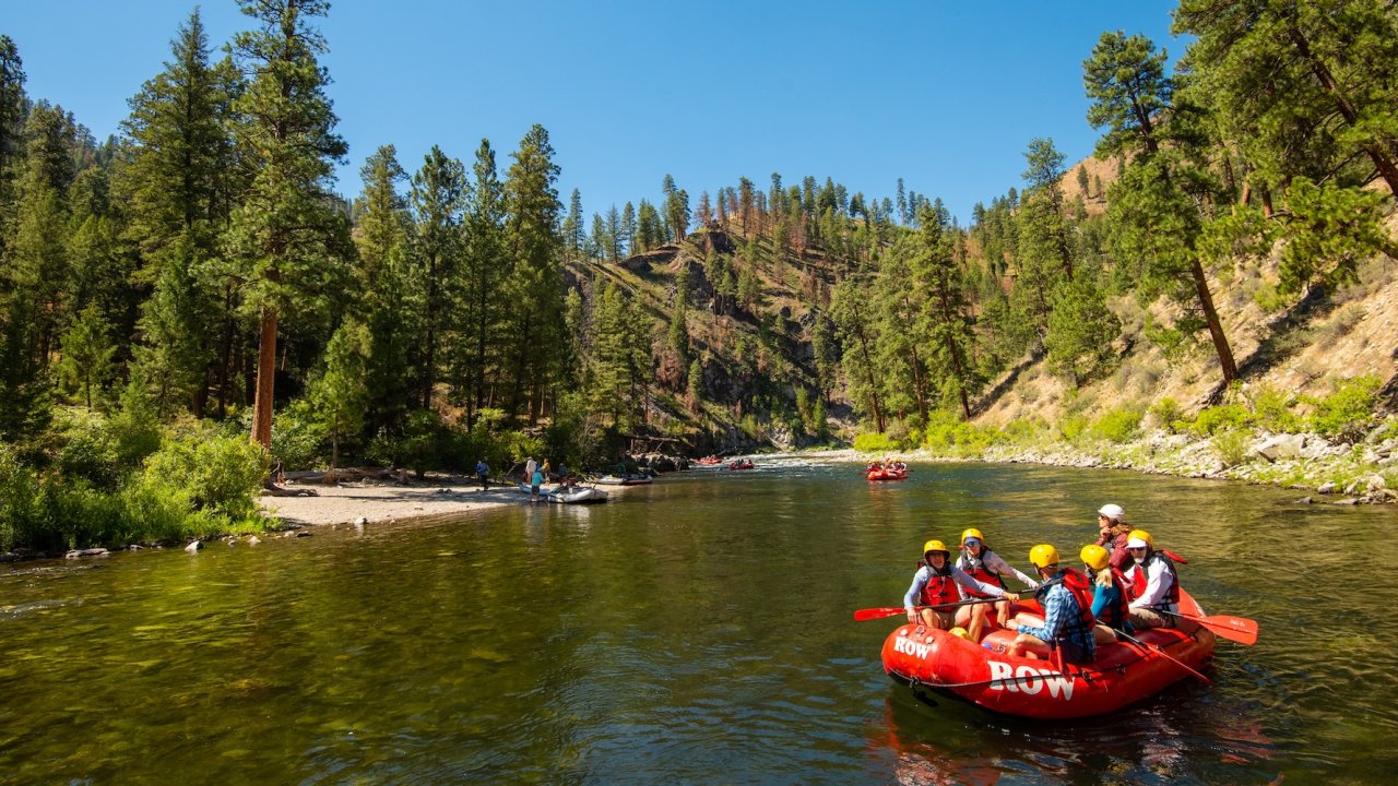 Group rafting on a calm stretch of river surrounded by pine-covered canyon hills.
