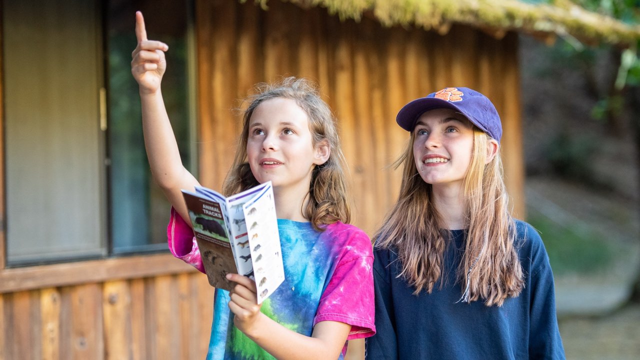 Two young girls learning about wildlife using an animal tracks guide during a nature-based education program in Idaho, supporting youth connection to the outdoors.