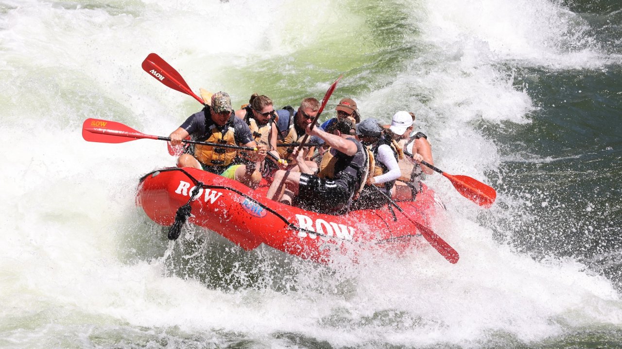A red ROW Adventures raft going through a splashy rapid on the Clark Fork river in Montana.
