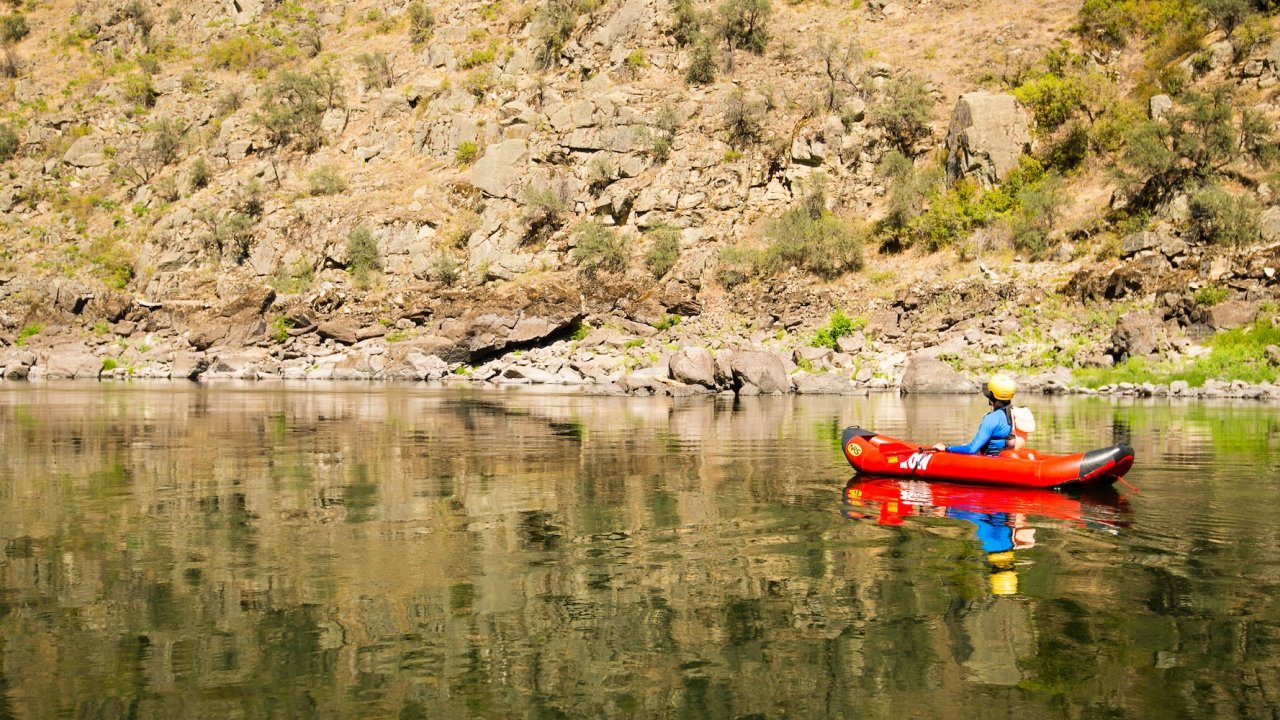 Solo paddler drifting on smooth reflective water beside rocky canyon slopes.