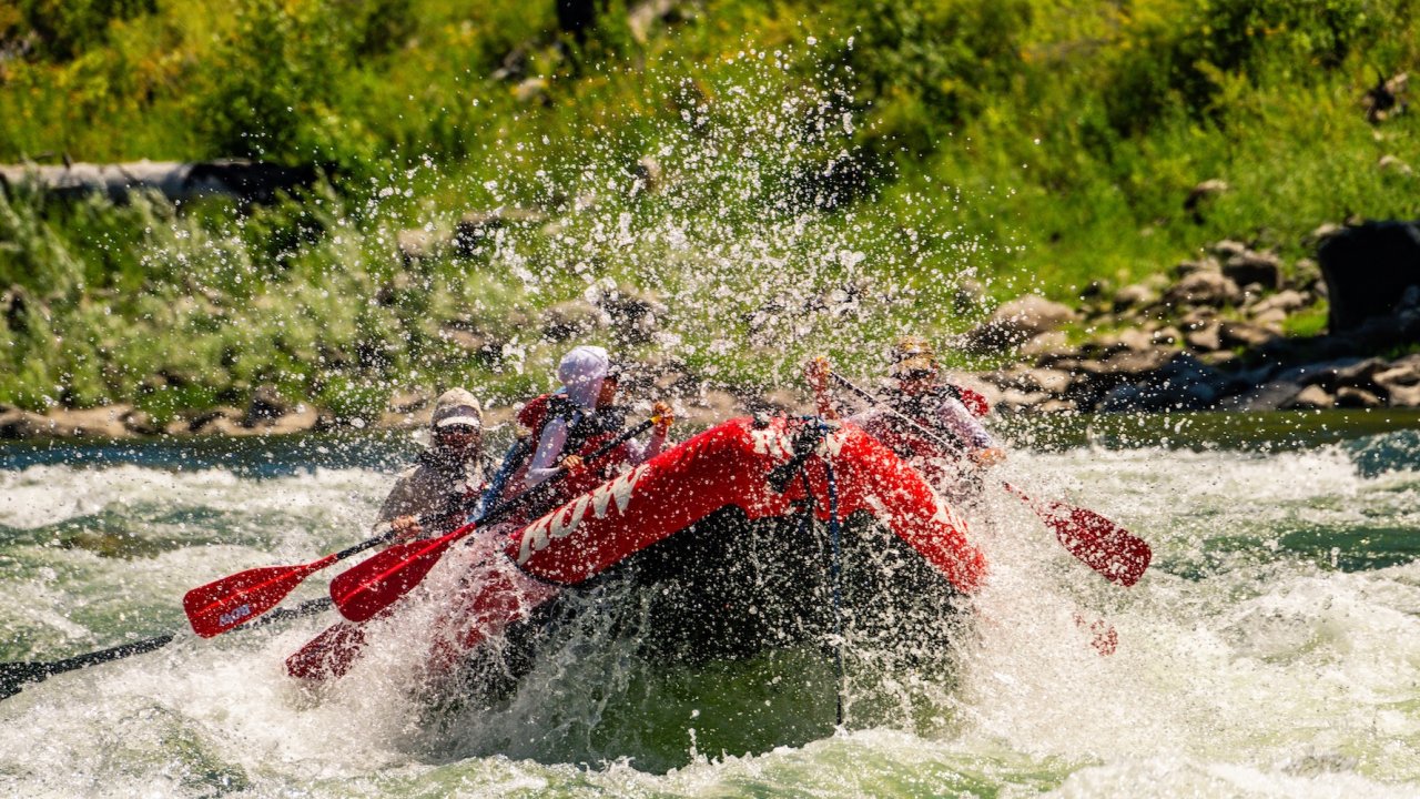 Raft powering through a splashy wave train with paddlers working together.