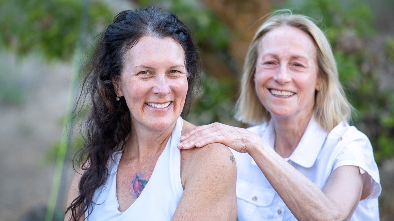 Two women smiling during a riverside wellness retreat in Idaho, where relaxation and connection are part of the whitewater rafting experience.