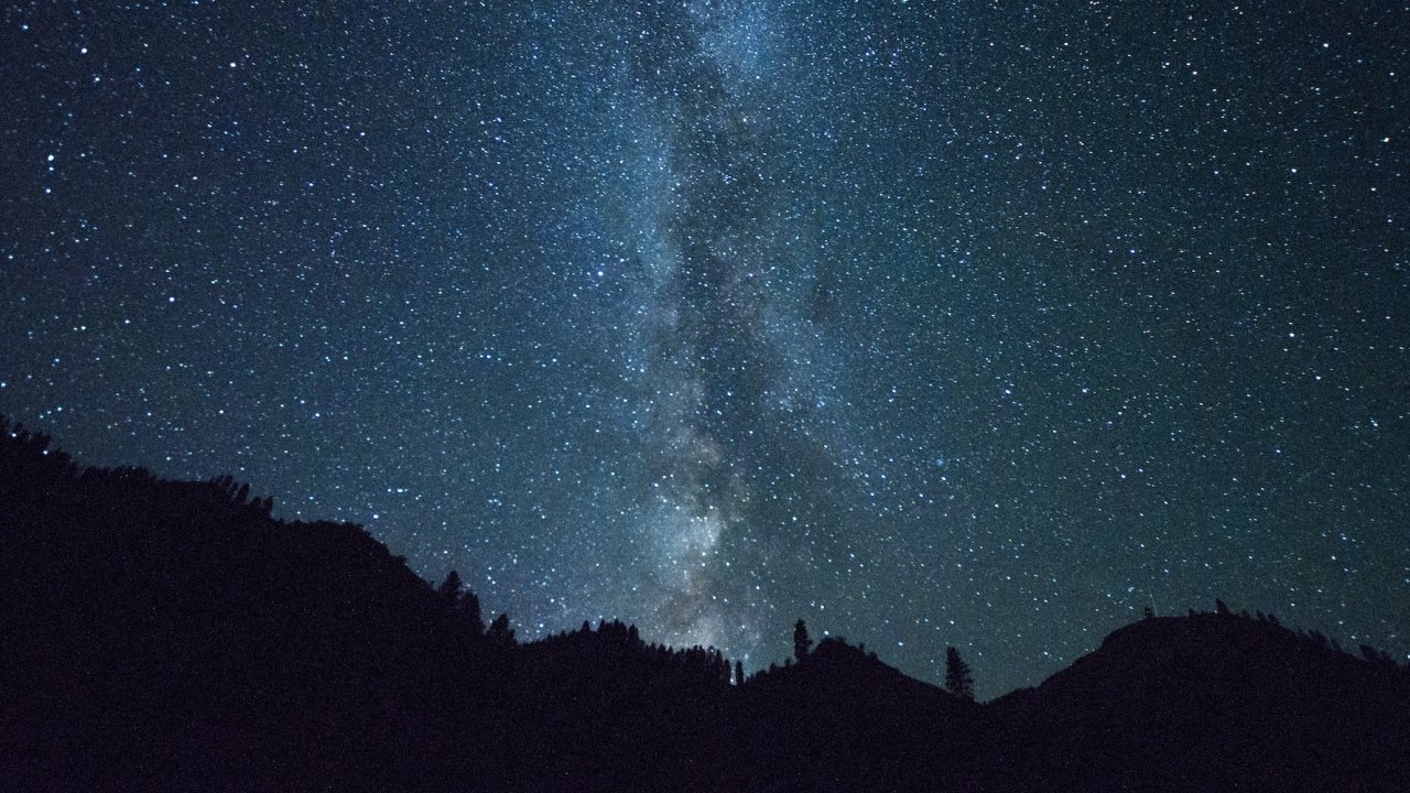 Star-filled night sky over dark mountain silhouettes along the river.