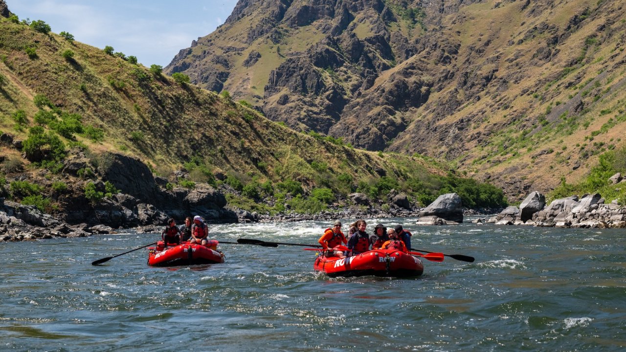 Two red rafts carrying guests through calm stretches of the Salmon River in Idaho, a whitewater rafting journey paired with wellness retreat elements.