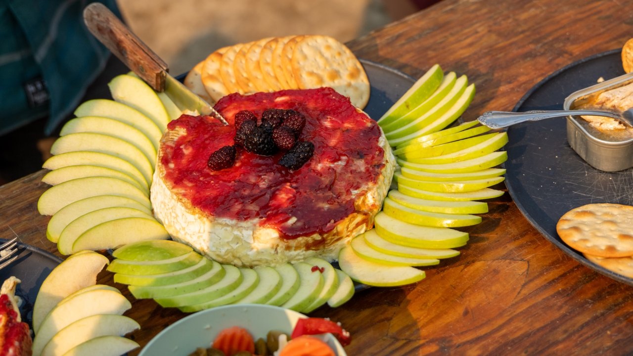 Baked brie with fruit and crackers served on a riverside camp table.