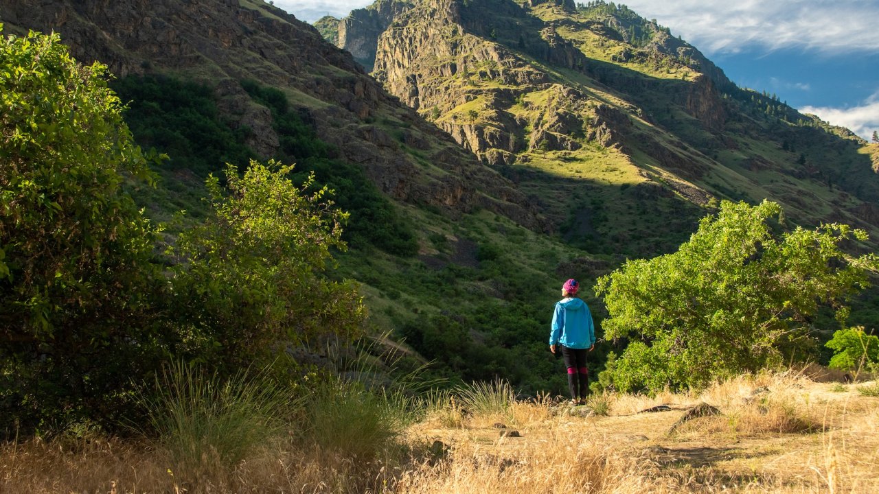 Adventurer standing in the rugged Idaho canyon landscape, surrounded by towering cliffs and lush greenery, embracing the restorative power of wellness travel.