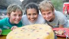 Kids smiling behind a pineapple upside down cake patiently waiting for a slice