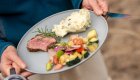 Person standing up holding a grey plate with steak, greek salad, and mashed potatoes