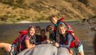 A group of kids gathered around the end of an upside down inflatable kayak in the river on the Lower Salmon River