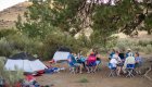 Guests on a multi-day rafting trip on the Deschutes gathered around the camping dinner tables enjoying a meal 