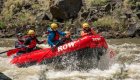 A red whitewater raft full of paddlers wearing yellow helmets paddling through a rapid in Idaho
