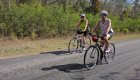 Two women riding their bikes on a paved road and smiling