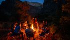 A group of people around a campfire at dusk while multi day rafting