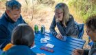 A group of people sitting around a blue table playing a game of cribbage