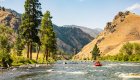 A red raft floating downstream towards the camera on the Middle Fork Salmon River on a sunny day