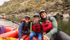 A dad and his two sons wearing red life jackets while on a red raft in Idaho