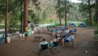 A group of people sitting in chairs listening to someone standing up and talking at a campsite along the Middle Fork Salmon River
