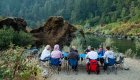 A group of people sitting around a row of blue tables enjoying dinner while camping along the Rogue River in Oregon
