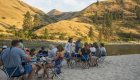 Guests sitting around camping tables for dinner on a sandy beach along the Lower Salmon River