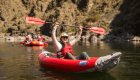 A person in an inflatable kayak holding the kayak paddle up in the air on the Lower Salmon River in Idhao