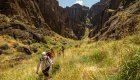 A group of people in a line hiking through a green field with towering canyon walls in Idaho