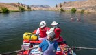 River guide rowing two guests on a red raft down the Deschutes River in Central Oregon