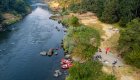 Drone shot of red boats tied up to shore with tents, tables and chairs sprawled across a sandy beach camp along the Rogue River in September