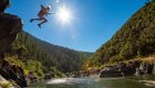 A girl jumping off a rock with the sun shining in the background into a rive