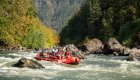 A red raft navigating through boulders in a river on a sunny day