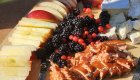 Picnic board with sliced apples, berries, cheese, and salmon in sunlight