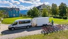 ROW Adventures support van and bike trailer parked near historic buildings in a scenic Idaho mountain setting, with guides unloading bikes for a cycling tour.