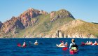 A small group paddles sea kayaks along Corsica’s rugged Mediterranean coastline during a guided Corsica tour.