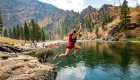 Rafter jumping from a rocky riverbank into calm green water with canyon scenery.