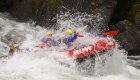A red raft full of paddlers in yellow helmets going through a large whitewater wave on the Lochsa River