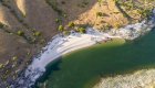 Aerial view of sandy riverside camp with tents and rafts along a clear green river.