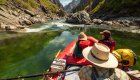 View from a raft floating through clear green water in a narrow mountain canyon.