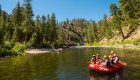 Group rafting on a calm stretch of river surrounded by pine-covered canyon hills.