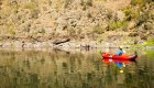 Solo paddler drifting on smooth reflective water beside rocky canyon slopes.