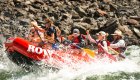 Group paddling through lively rapids beside a rocky riverbank.