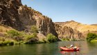 red raft floating on the Deschutes river in front of basalt columns that line the river