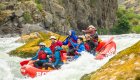 red whitewater raft with paddlers passing through large rocks on river