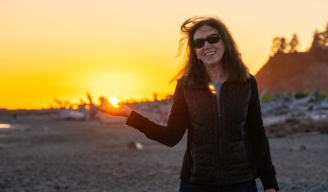 Traveler enjoying sunset at a beach on the Olympic Peninsula, Washington, with driftwood and golden skies along the Pacific coast.