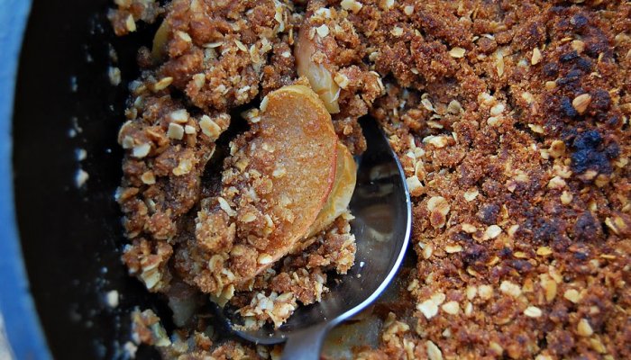 apple crisp being served with a spoon from a dutch oven 
