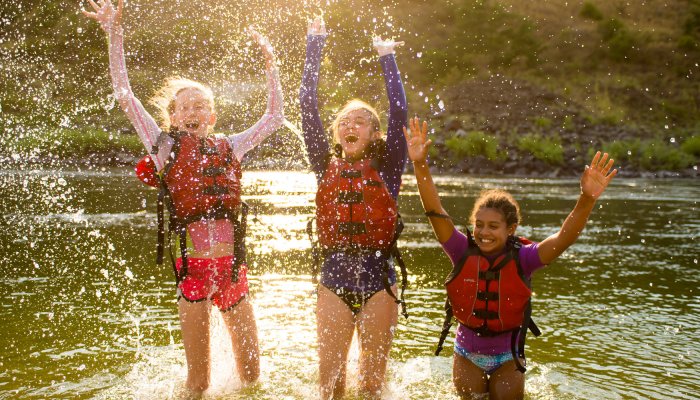 three girls splashing in a river with red pfds on