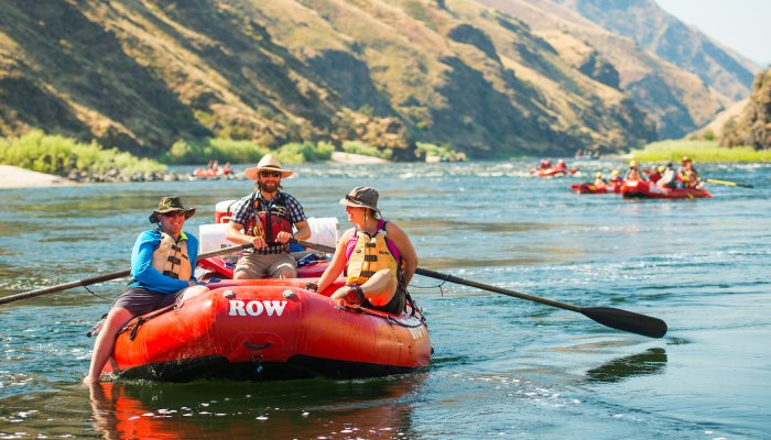 Two guests lounging on a red raft while their guide rows them downstream on a sunny summers day