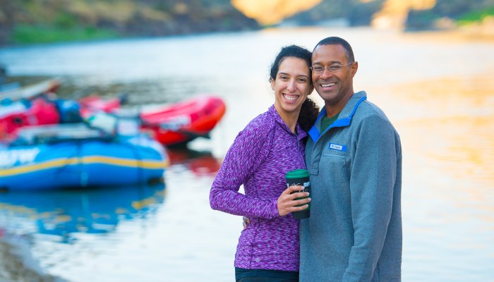 A couple smiling for a photo while camping along a sandy beach on the Salmon River
